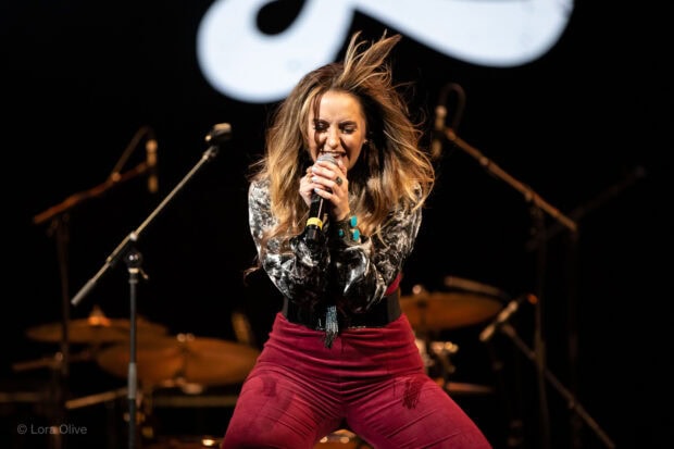 Lainey Wilson performing energetically on stage with a microphone in a live concert setting