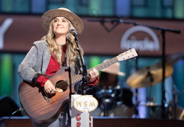 Lainey Wilson performing live on stage with a guitar and wearing a hat