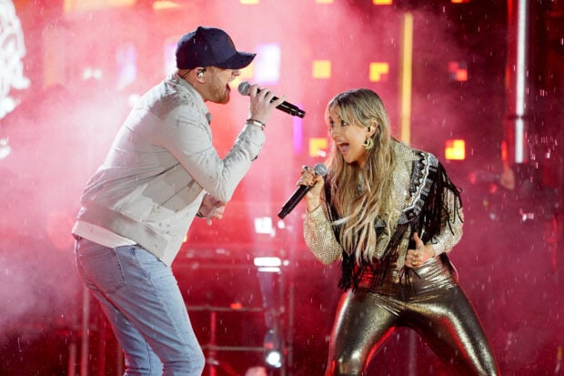 Lainey Wilson performs on stage with a male singer during a live concert in the rain