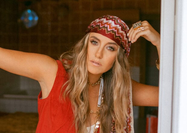 Lainey Wilson wearing a red sleeveless top and patterned headscarf looking thoughtfully