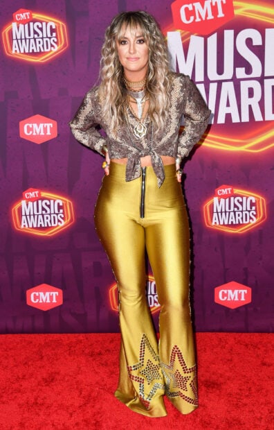 Lainey Wilson wearing shiny gold pants and a patterned top posing on the red carpet