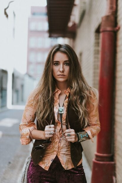 Young woman with long hair wearing a vintage vest and rings outdoors in an urban setting