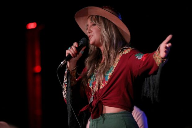 Lainey Wilson singing on stage wearing a hat and colorful outfit
