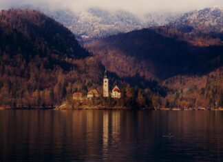 A peaceful view of Lake Bled with a church on the island surrounded by autumn forests and calm water