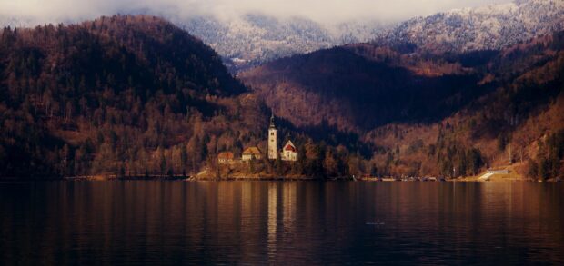 A peaceful view of Lake Bled with a church on the island surrounded by autumn forests and calm water