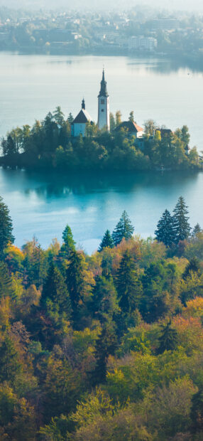 Autumn forest and historic church on island in Lake Bled surrounded by clear blue water