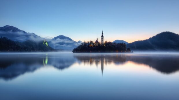 Misty lake Bled with church island and mountains reflecting on calm water at dawn