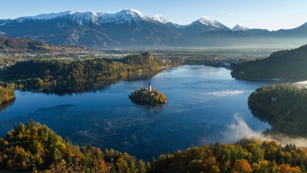 Scenic view of Lake Bled with snow capped mountains and autumn trees in Slovenia