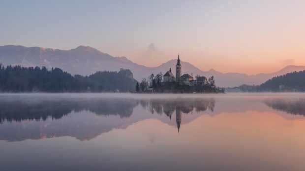 Serene view of Lake Bled with church on the island and mountains in the background at sunrise