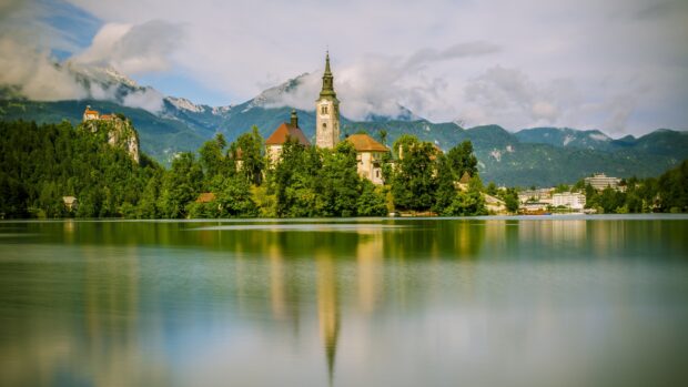 The Island Church surrounded by forest on Lake Bled with mountains in the background