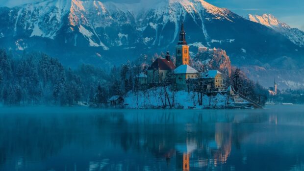 Winter scene with Lake Bled church surrounded by snow covered trees and mountains