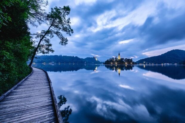 Tranquil Lake Bled view with calm water and a wooden walkway under cloudy skies