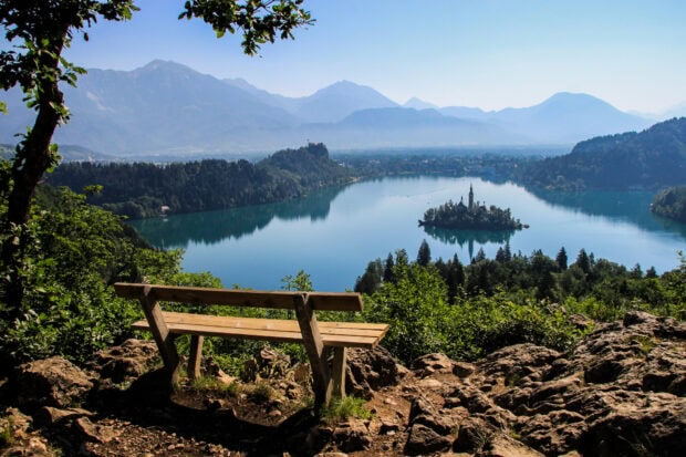 A wooden bench overlooking the serene Lake Bled surrounded by mountains and greenery