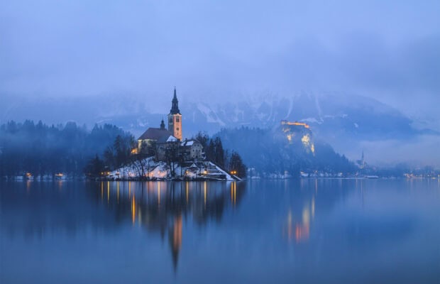 Lake Bled island with a church and snowy surroundings in winter mist