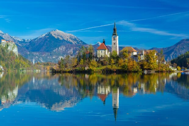 A serene view of Lake Bled featuring the island with a church surrounded by autumn trees and mountains