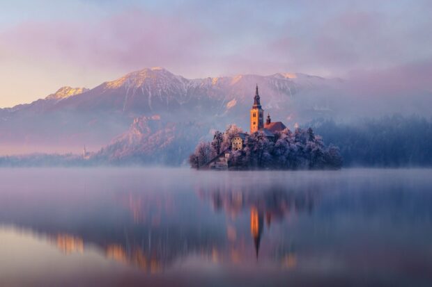 Lake Bled with misty island and church surrounded by snowy mountains in winter