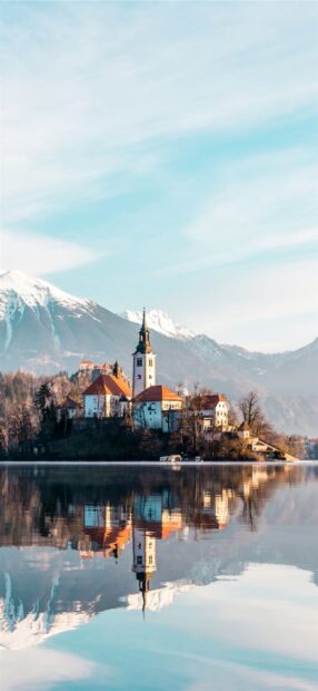 Beautiful lake Bled scene with a church reflected in the calm water and snowy mountains in the background