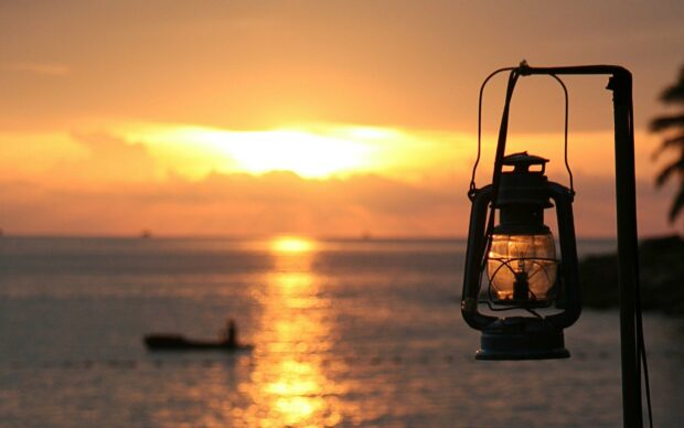 A vintage lantern hanging near the ocean during a warm sunset with calm waters and a boat in the distance