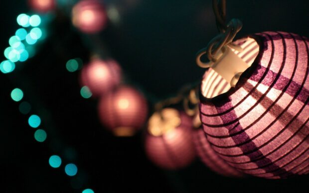 A close up of purple lanterns glowing softly in the dark night with blurred lights in the background