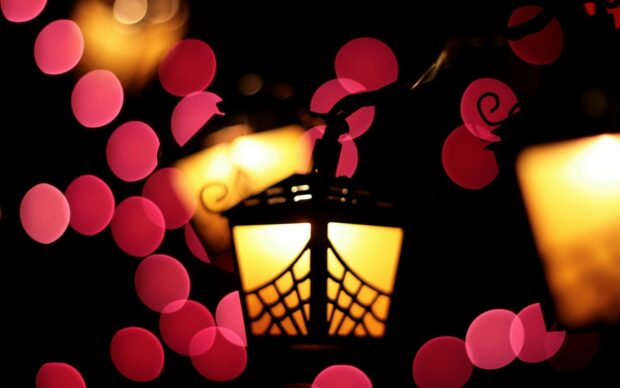 A glowing lantern with intricate cutouts surrounded by red bokeh lights