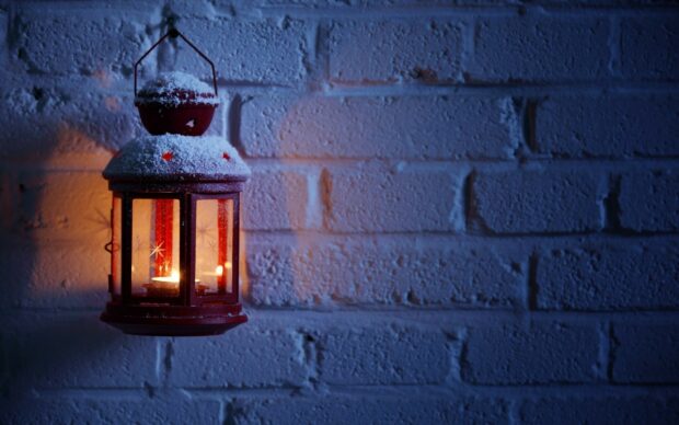 A red lantern covered with snow glowing against a blue brick wall in winter night