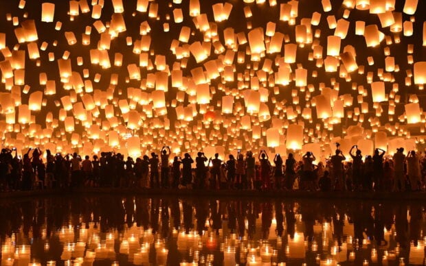 A crowd of people releasing lanterns during a nighttime lanterns festival reflected on water