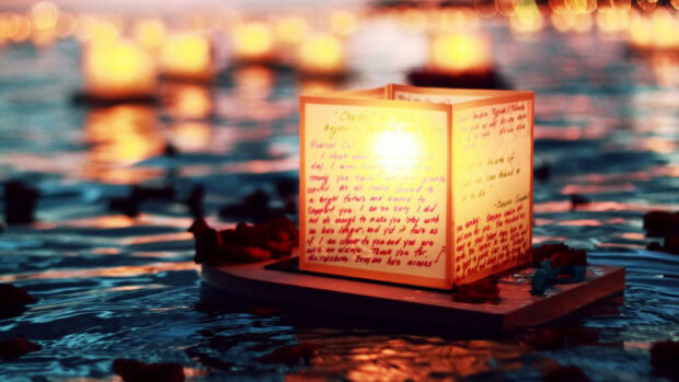 A glowing lantern floating on water with written messages in a peaceful night setting