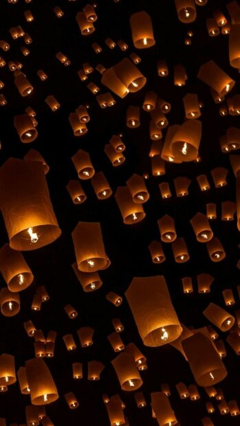 Orange lanterns glowing and floating in the night sky during a festival celebration
