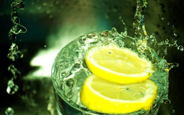 Two lemon slices splash into a glass of water creating refreshing motion