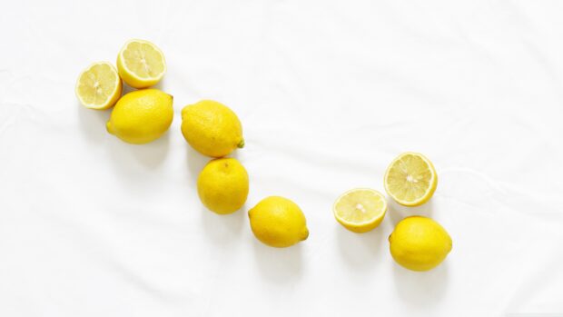 Fresh lemons arranged on a white surface in a curved line with some cut in half