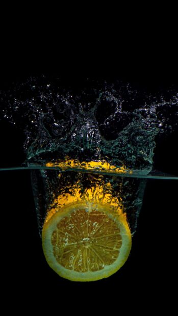 A lemon slice splashing into water with bubbles and ripples on black background