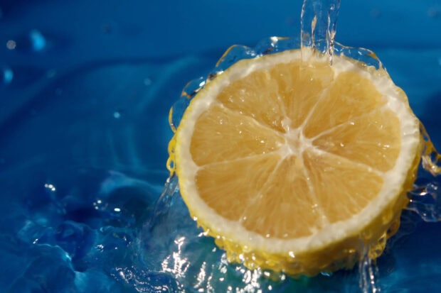 Fresh lemon slice falling into water with vibrant blue background