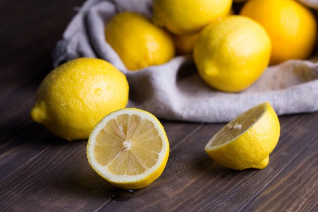 A close up of lemon slices and whole lemons on a wooden table with a cloth in the background