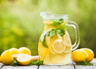 A refreshing pitcher of lemonade with fresh lemon slices and mint leaves on a wooden table