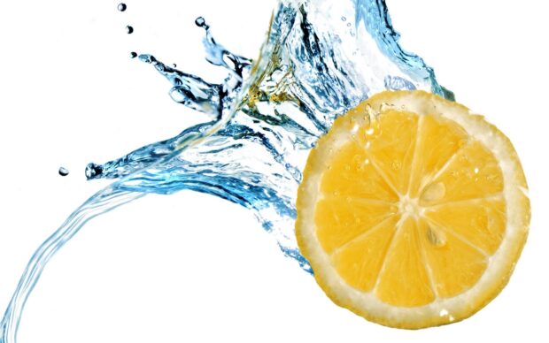 Fresh lemon slice splashing into clear water with vibrant yellow color