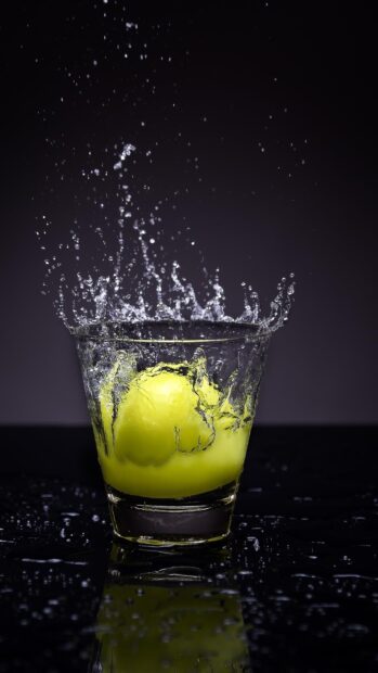 A lemon dropping into a glass of water creating a splash with water droplets everywhere