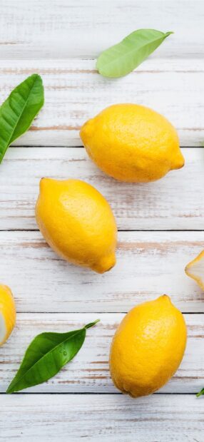 Fresh lemons and green leaves on wooden surface with lemon texture