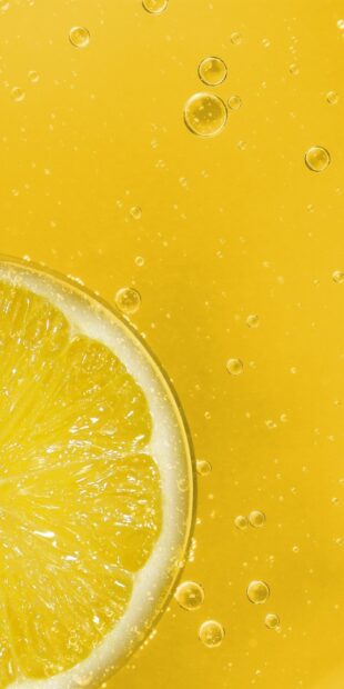 A close up of a lemon slice with bubbles in a yellow liquid