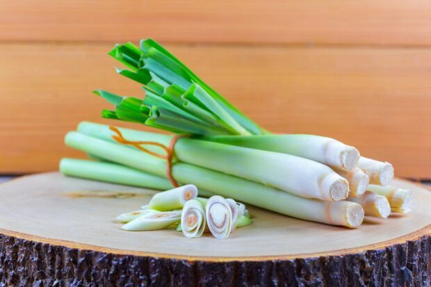 Fresh lemongrass stalks and sliced lemongrass on a wooden surface with green leaves