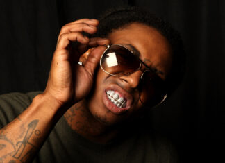 Lil Wayne adjusting his sunglasses showing diamond grill with visible tattoos