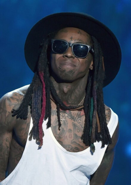 Lil Wayne with colorful dreadlocks and sunglasses performing on stage