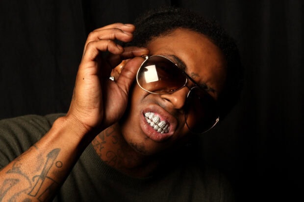 Lil Wayne adjusting his sunglasses showing diamond grill with visible tattoos