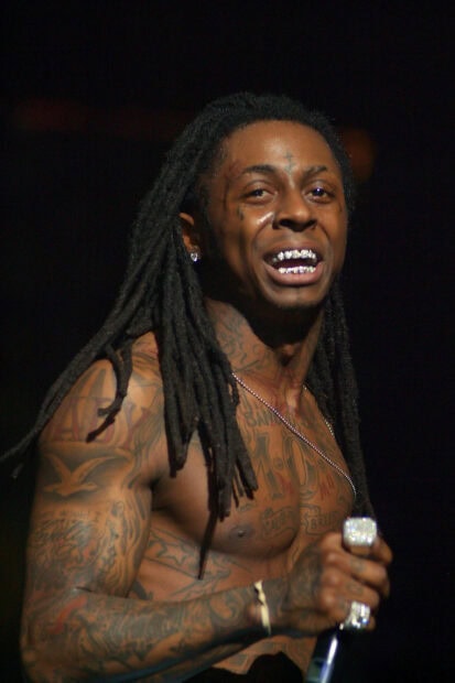 Lil Wayne with tattoos and dreadlocks performing on stage with a microphone