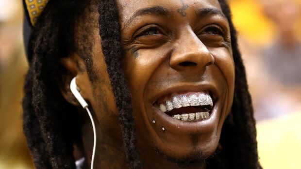 Lil Wayne showing his diamond grills with earphones in a close up smile
