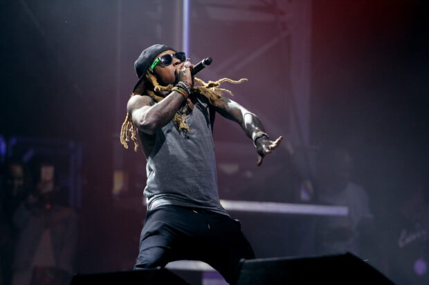 Lil Wayne performing live on stage with dreadlocks and sunglasses in a concert setting