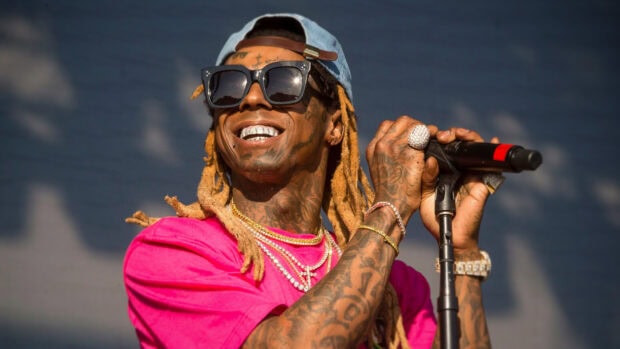 Lil Wayne with dreadlocks and tattoos smiling while holding a microphone on stage