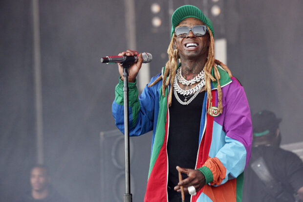 Lil Wayne wearing colorful jacket and chains holding a microphone on stage during a performance