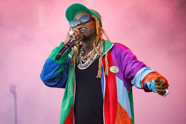 Lil Wayne wearing colorful jacket and green cap performing on stage