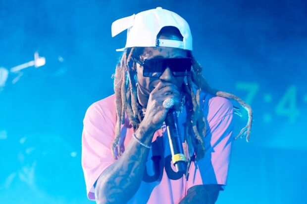 Lil Wayne wearing sunglasses and a white cap performing on stage with a microphone