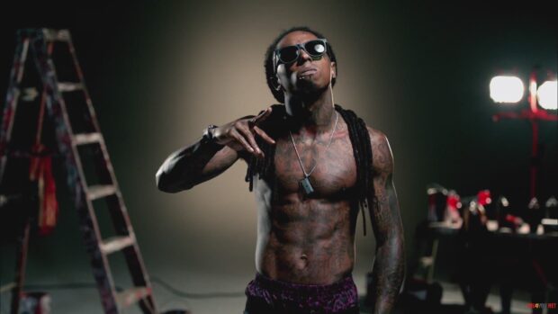 Lil Wayne performing with tattoos and sunglasses in a studio setting